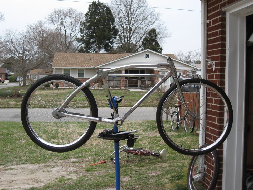 Chrome bicycle frame on repair stand, with another bicycle visible in background