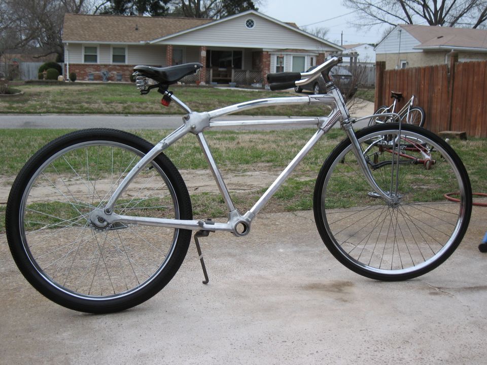Custom bicycle with chrome frame and black seat, parked on concrete in front of a house. Another bicycle is visible behind it
