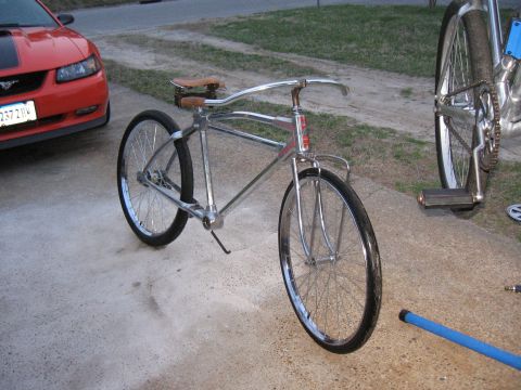 Chrome bicycle with brown leather seat and red car in background