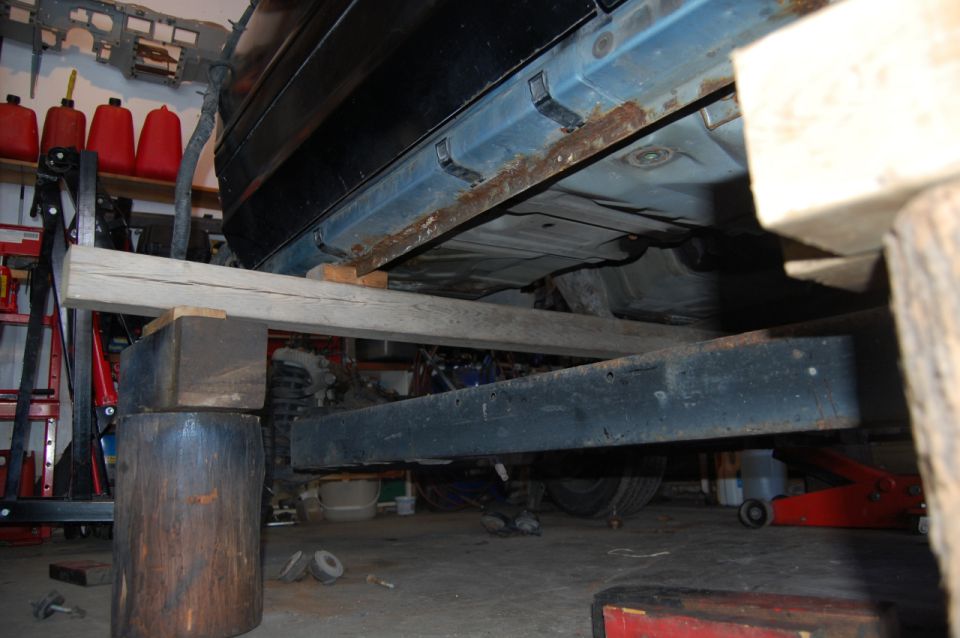 car body supported by wood blocks and beams, showing rusty rocker panel