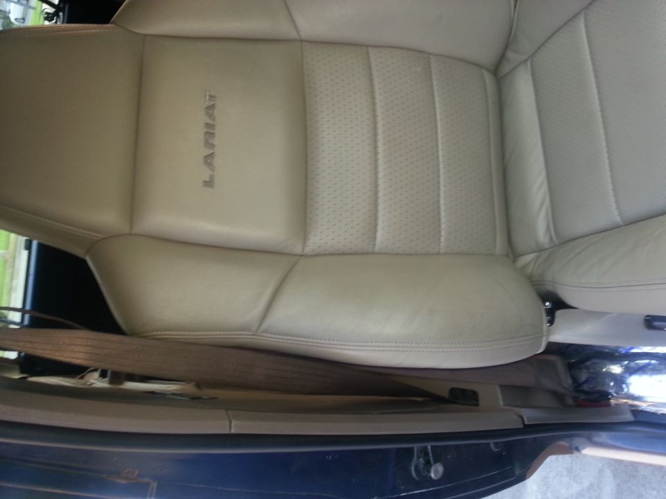 Close-up of a tan leather car seat with 'LARIAT' embossed on the side. Seatbelt is visible