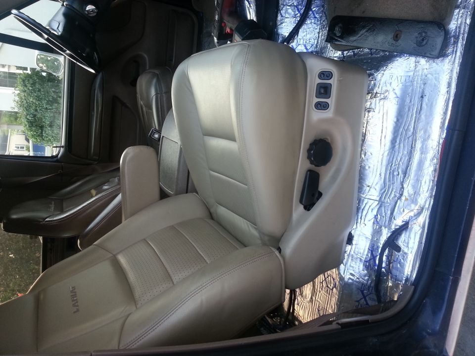Interior shot of a vehicle showing tan leather seats and the steering wheel. The floor is covered in insulation