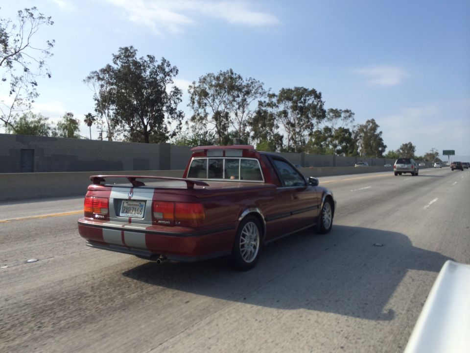 Red pickup truck with silver racing stripes on the rear, driving on a highway