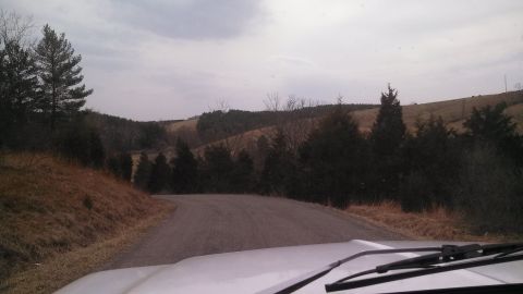 1979 Ford Bronco - View from inside a vehicle driving on a rural road with rolling hills and trees.
