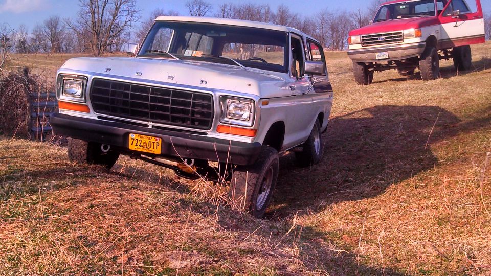 White 1978 Ford Bronco in foreground, red and white Ford Bronco in background on grassy hill