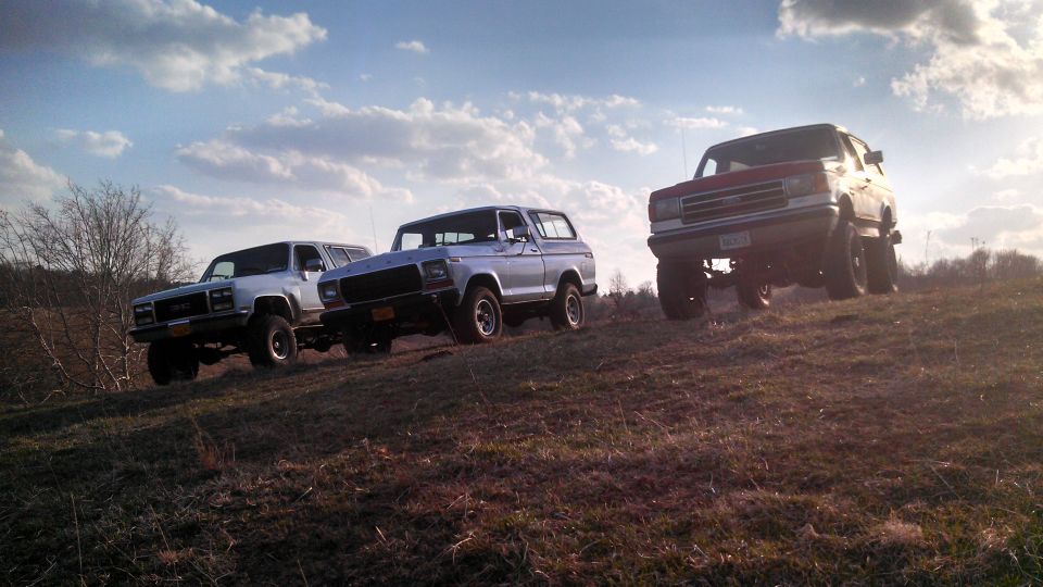 Silver 1979 Ford Bronco driving up a hill with two other SUVs