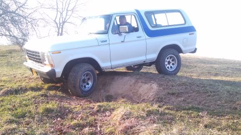 1979 Ford Bronco - A white and blue Ford Bronco navigates a dirt embankment on a sunny day.