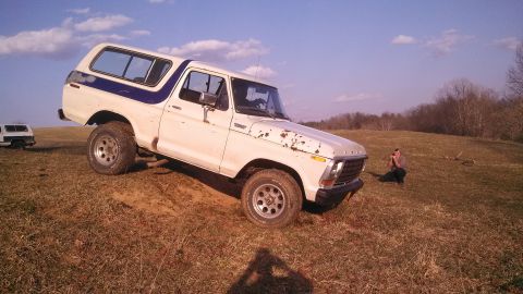 1979 Ford Bronco - White 1979 Ford Bronco with blue stripe on a dirt and grass hill.