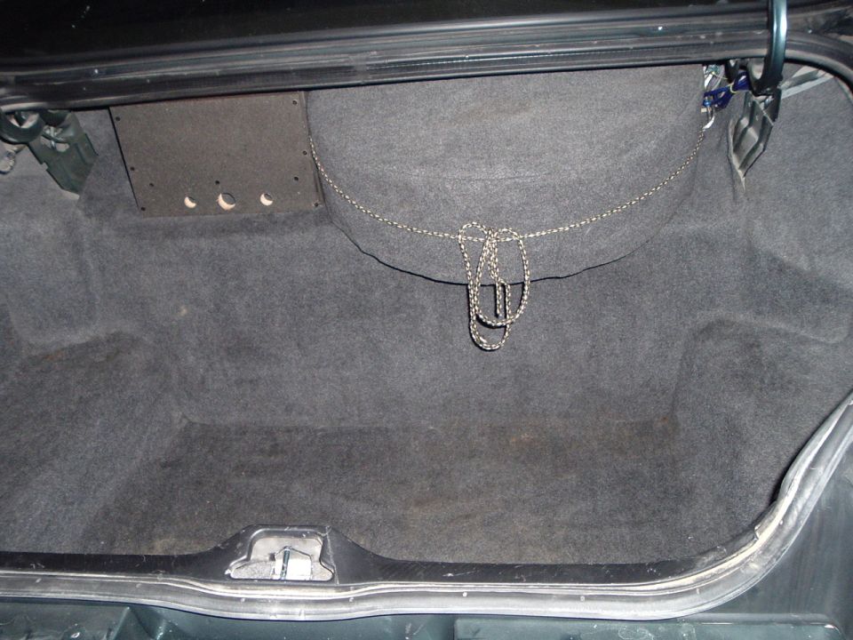 Empty carpeted car trunk interior with tie-down chain, lid open