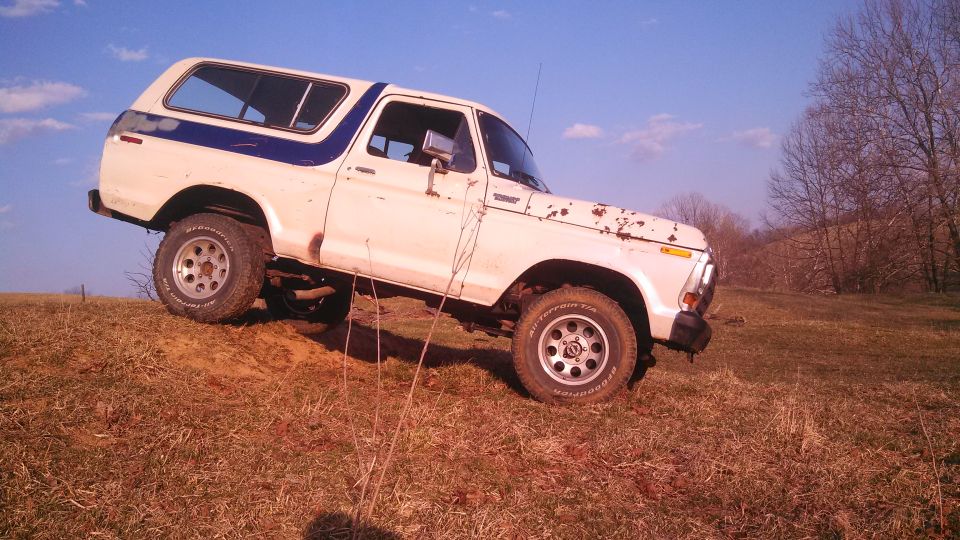 White Ford Bronco with blue stripe driving on a dirt hill