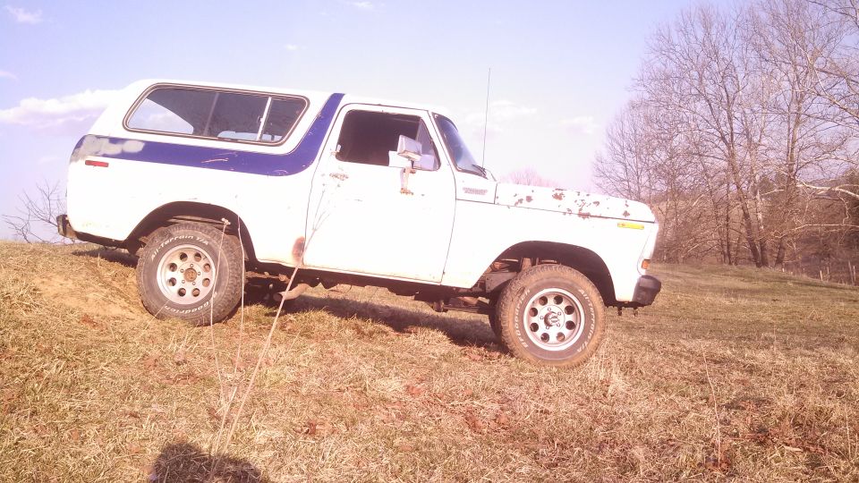 White and blue Ford Bronco on a grassy hill, showing rust and wear