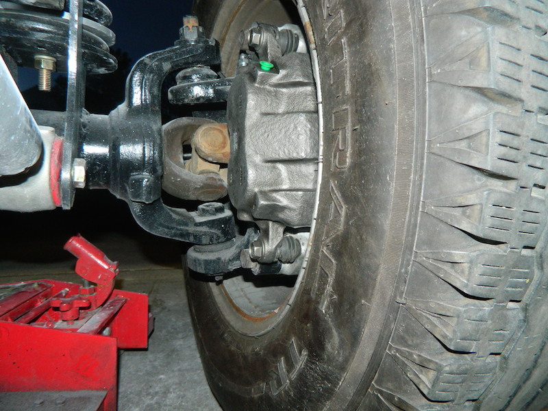 close-up of a vehicle's front brake caliper and tire assembly, with a red jack visible below