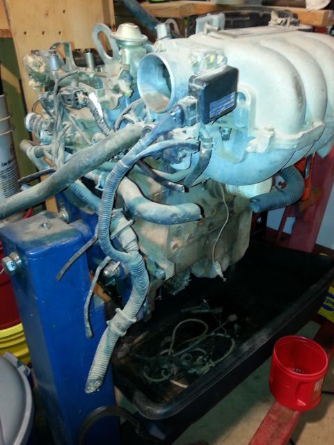 1991 Ford Festiva - Engine assembly, likely removed from a vehicle, is supported by a stand and surrounded by various automotive parts and tools.
