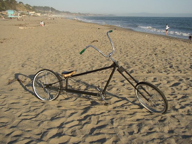 Black custom chopper bicycle with extended fork on a sandy beach by the ocean