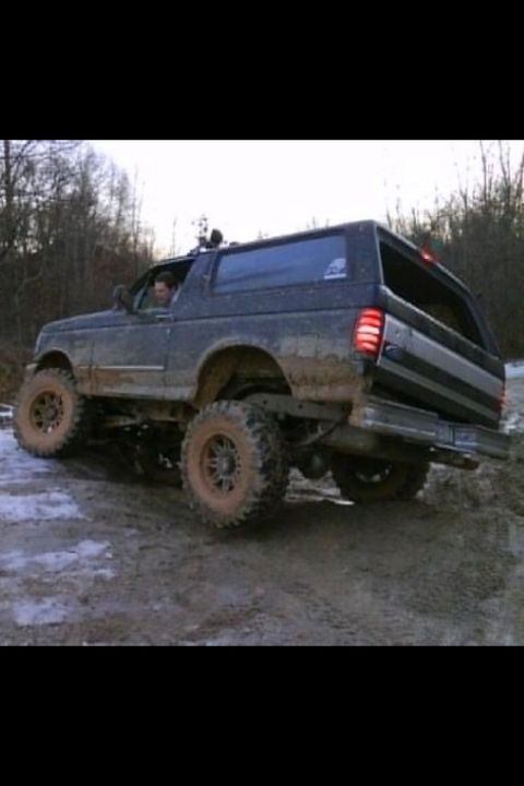 1995 Ford Bronco - Muddy 1995 Ford Bronco navigates an off-road trail with a driver inside.
