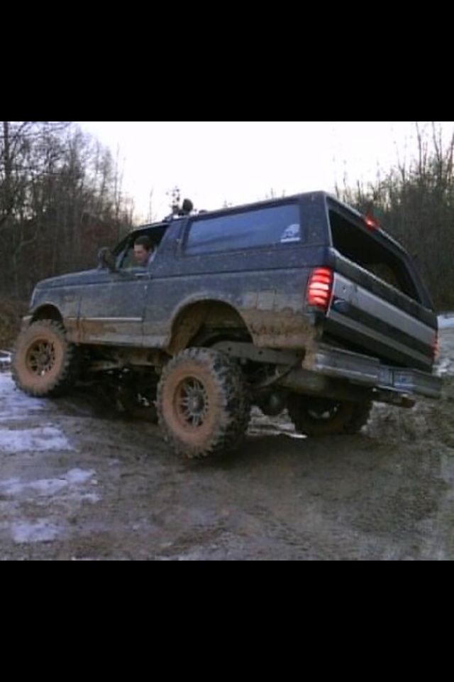 1995 Ford Bronco lifted and muddy driving on a dirt trail