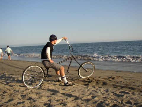 1989 Ford Bronco - A person rides a custom bicycle on the sand near the ocean waves.