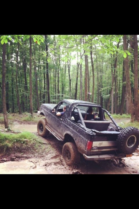 1995 Ford Bronco - This Ford Bronco is navigating a challenging muddy path through a dense forest.