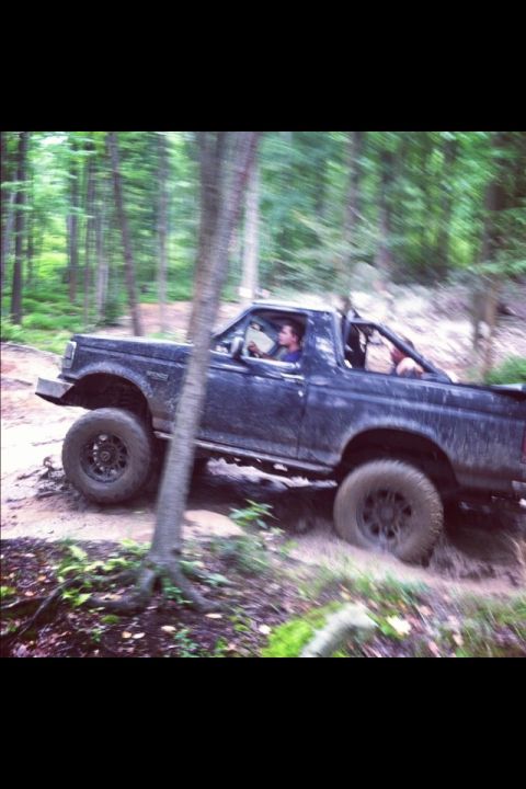 1995 Ford Bronco - A dark blue Ford Bronco navigates a muddy trail through a dense forest.