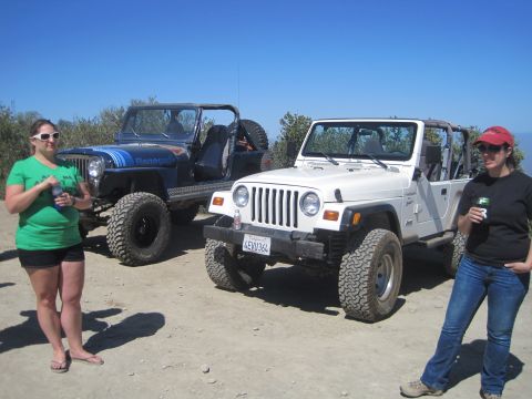 1989 Ford Bronco - Two women stand next to two Jeep Wranglers parked on a dirt road under a clear blue sky.