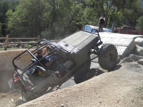 1989 Ford Bronco - An off-road Jeep Wrangler navigates a challenging course, tilting precariously as it moves over rocks and dirt.