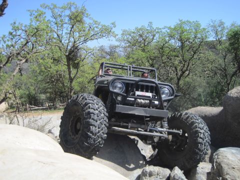 1989 Ford Bronco - This heavily modified Jeep Wrangler is shown tackling a rocky trail with two occupants visible.