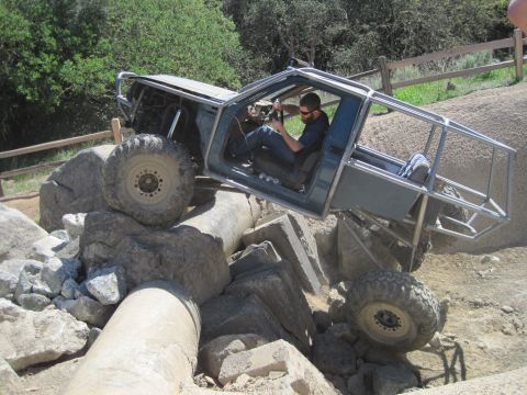 1989 Ford Bronco - A driver maneuvers a heavily modified off-road vehicle over large rocks and concrete debris.
