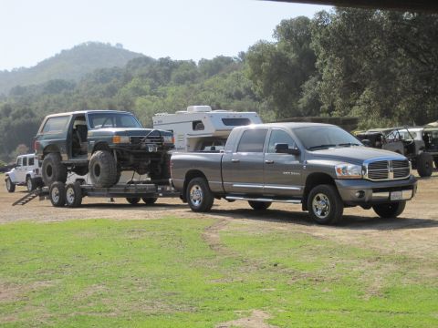 1989 Ford Bronco - A heavily modified green Ford Bronco is transported on a trailer by a grey Dodge Ram pickup truck.