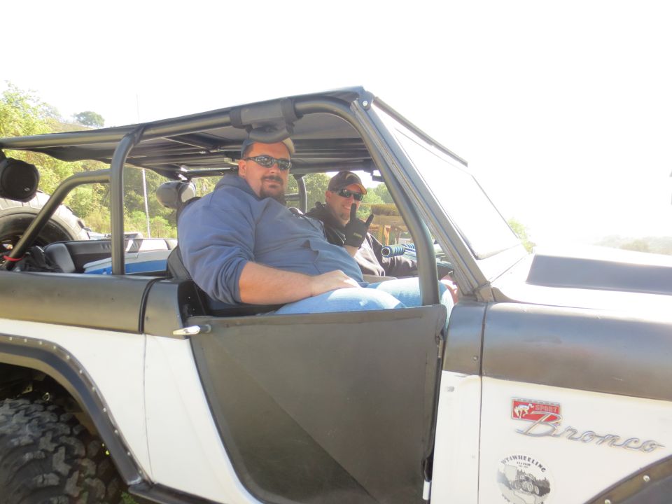 1989 Ford Bronco with two men inside, off-road tires visible