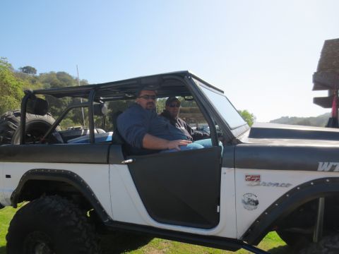 1989 Ford Bronco - A modified Ford Bronco with two occupants sits parked outdoors under a clear sky.