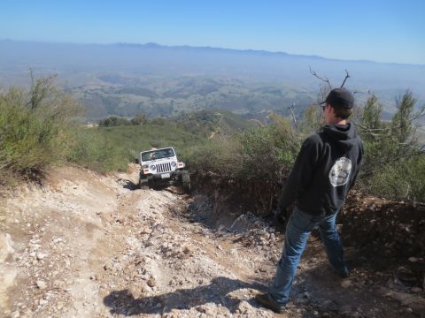 1989 Ford Bronco - A white Jeep navigates a steep, rocky off-road trail in a mountainous landscape.