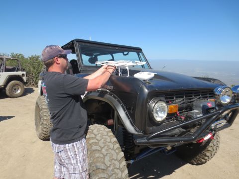 1989 Ford Bronco - A man prepares a drone for flight next to a modified Ford Bronco, with another off-road vehicle visible in the background.