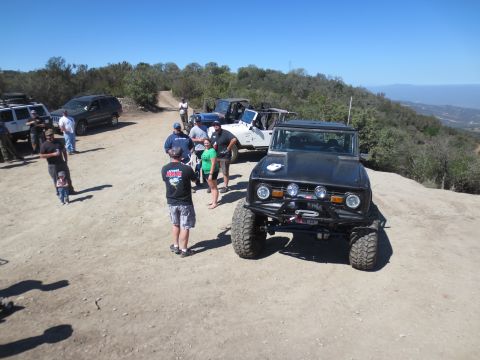 1989 Ford Bronco - A group of people and several off-road vehicles gather on a dusty trail overlooking a valley.