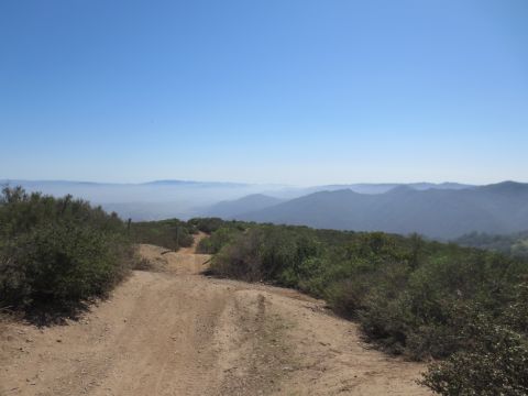 1989 Ford Bronco - A dirt road leads through a landscape of brush and hills towards a distant, hazy mountain range.