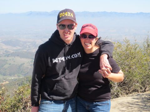 1989 Ford Bronco - A couple smiles for a photo while wearing hats and hoodies with text, with a hazy landscape behind them.