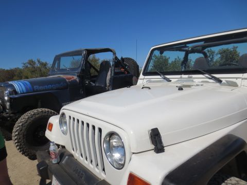 1989 Ford Bronco - Two Jeeps, a white Wrangler and a black CJ Renegade, are parked outdoors under a clear blue sky.