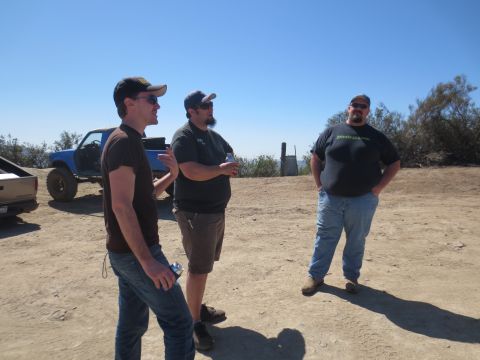 1989 Ford Bronco - A lifted blue pickup truck is visible in the background as three men converse outdoors.