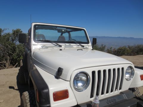 1989 Ford Bronco - This white Jeep Wrangler is parked on a dirt road with a scenic mountain view.