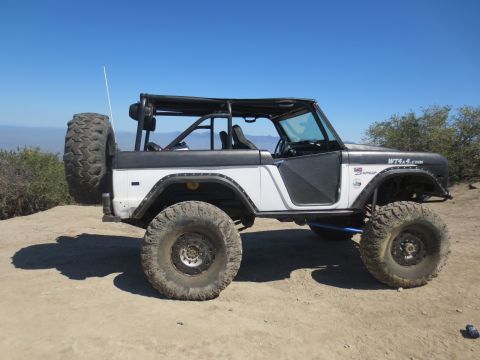 1989 Ford Bronco - This modified Ford Bronco is parked on a dirt road with a scenic view of hills and a clear blue sky.
