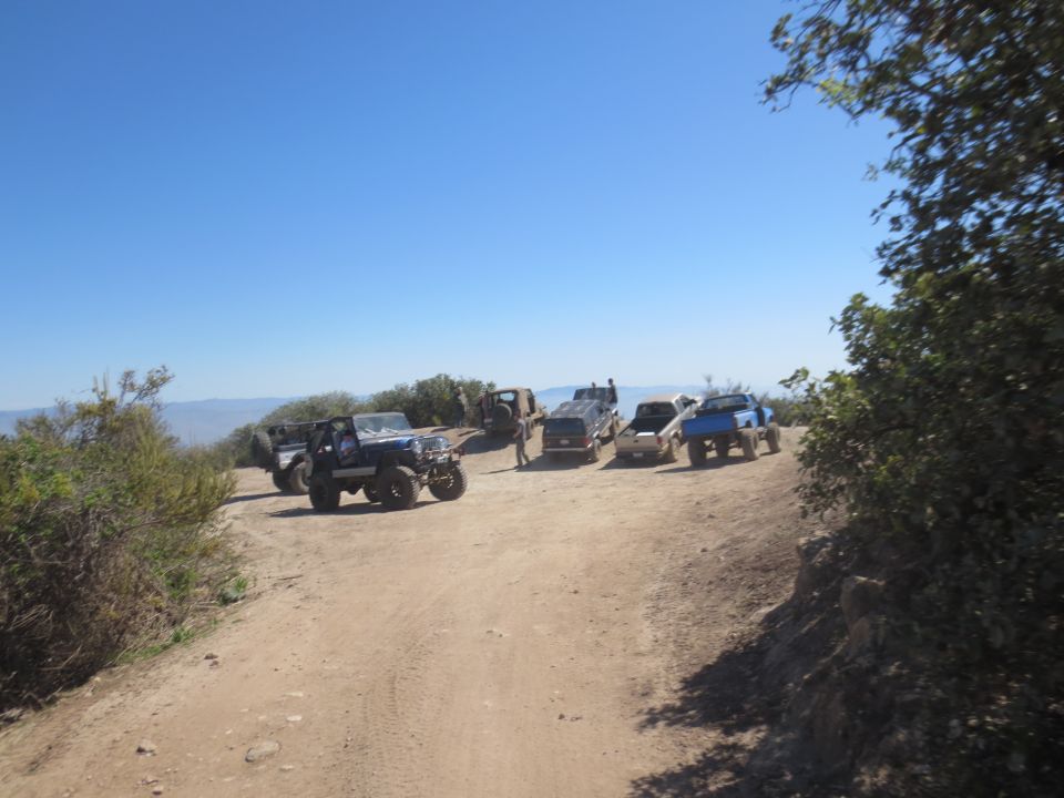 Several off-road vehicles parked on a dirt road with a clear blue sky