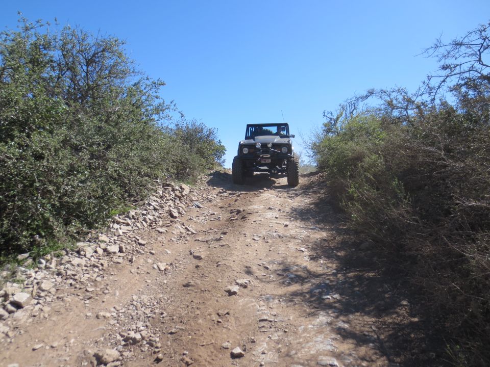 Black off-road vehicle with large tires driving up a rocky dirt path