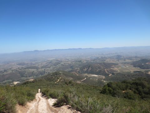1989 Ford Bronco - A scenic view of rolling hills and distant mountains, with a dirt path winding through the foreground vegetation.