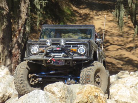 1989 Ford Bronco - A black Ford Bronco is shown off-roading on a dirt path with large rocks.
