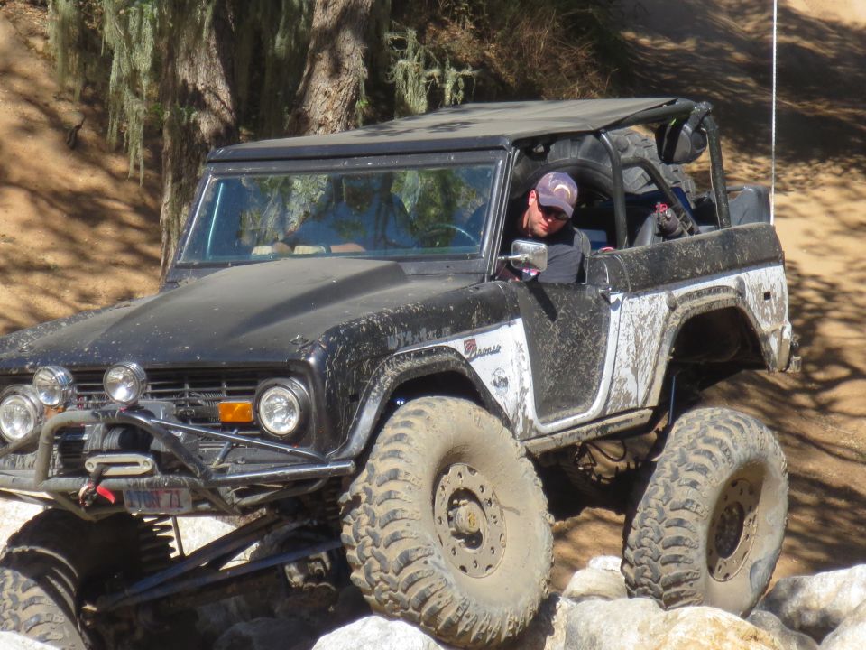 Black and white Ford Bronco with large tires off-roading over rocks