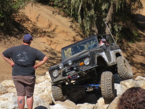 1989 Ford Bronco - A black Ford Bronco navigates a rocky off-road course with a person watching.