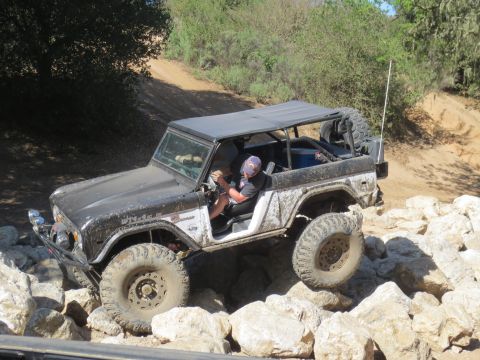 1989 Ford Bronco - A Ford Bronco is shown off-roading over rocks on a dusty trail.