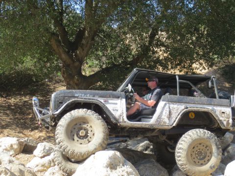 1989 Ford Bronco - A heavily modified black Ford Bronco navigates a rocky trail with a driver behind the wheel.