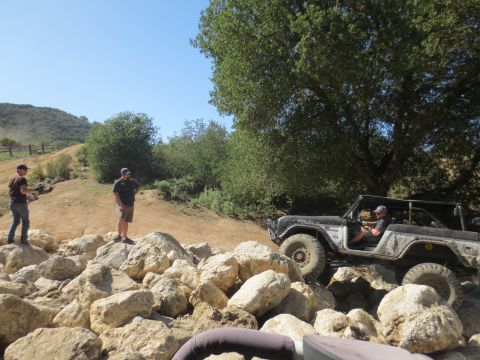 1989 Ford Bronco - A 1989 Ford Bronco is shown off-roading over a pile of large rocks on a sunny day.