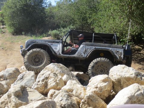 1989 Ford Bronco - A black Jeep Wrangler navigates a rocky terrain on a sunny day.