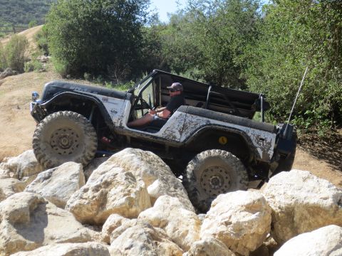 1989 Ford Bronco - A Jeep CJ-7 is shown off-roading over a challenging rocky path.